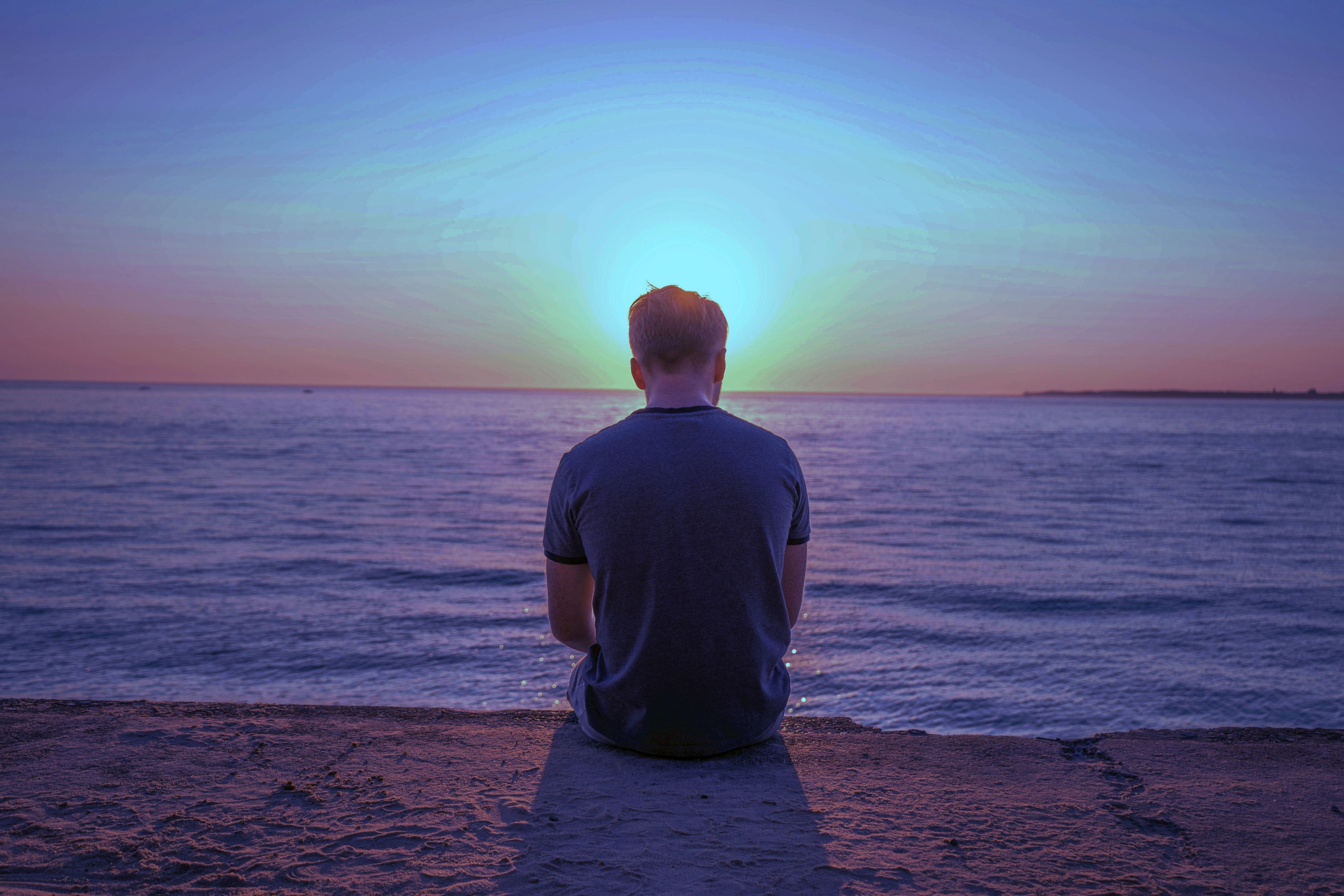 man sitting on sand front of sea during golden hour