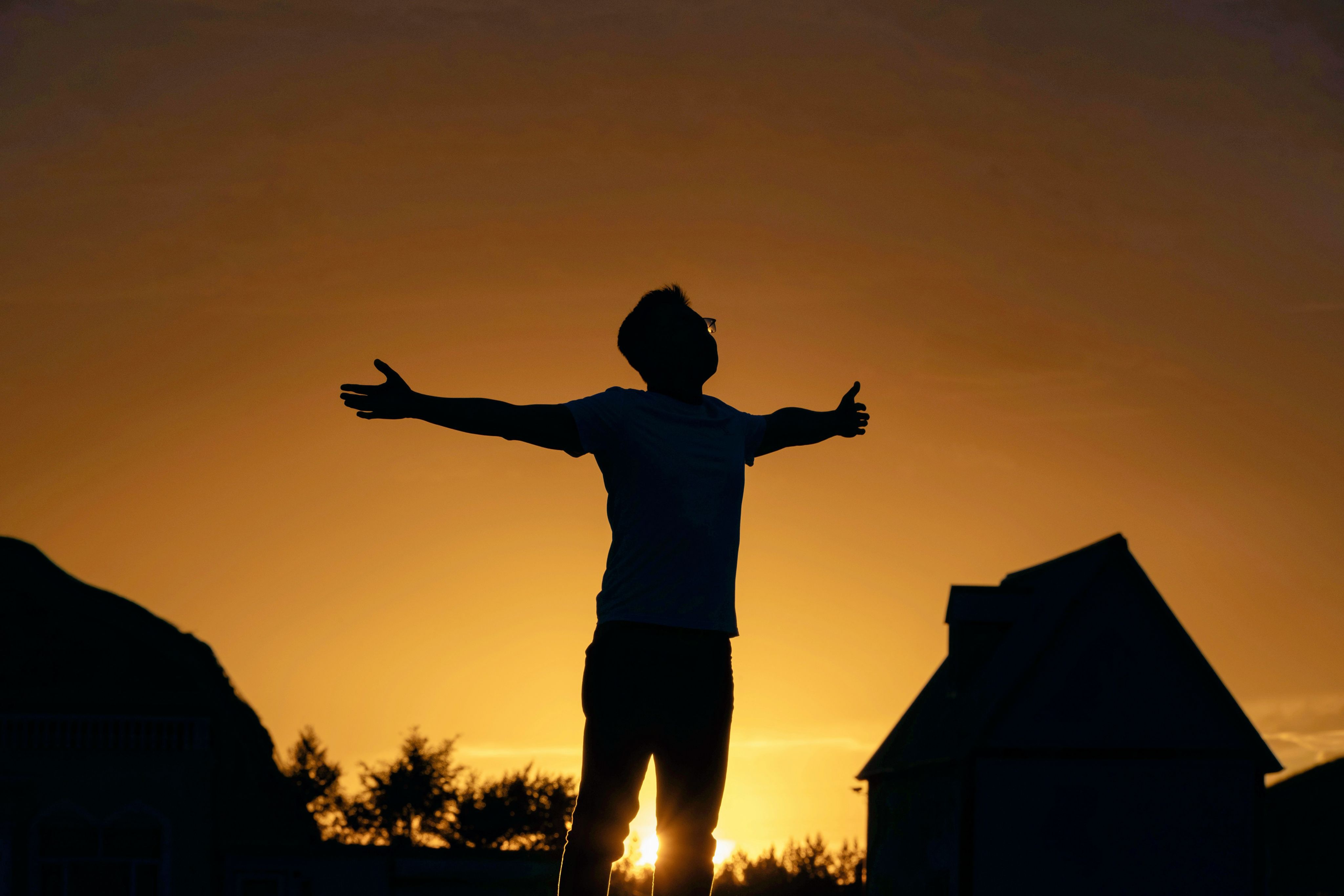 Man embraces the sunset with outstretched arms.